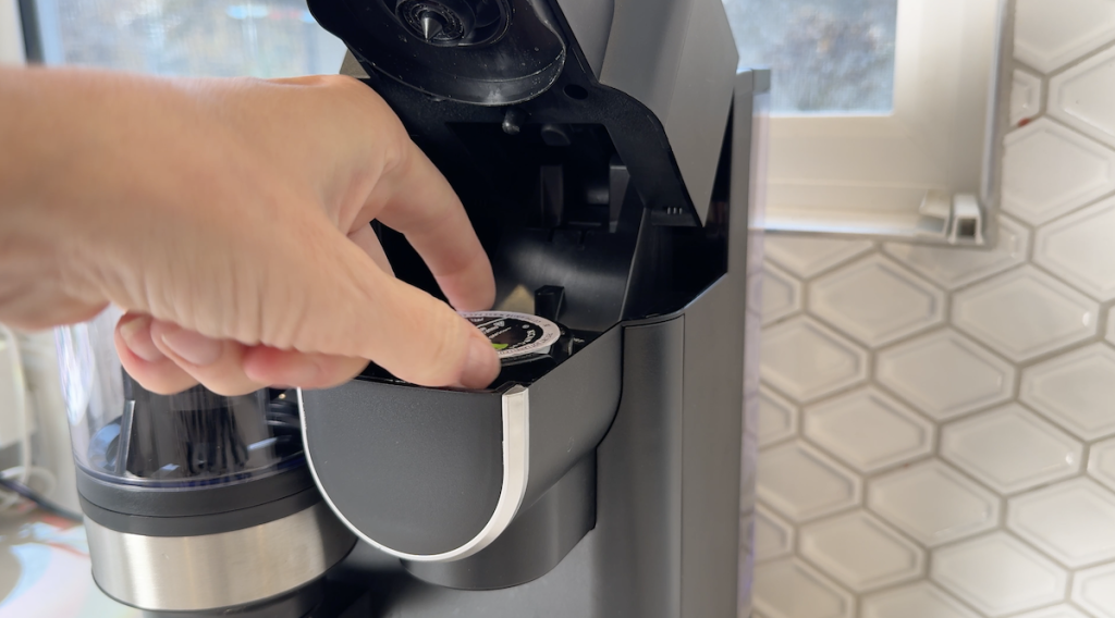 Close up of Erin's hand placing a K-cup into the machine to brew.