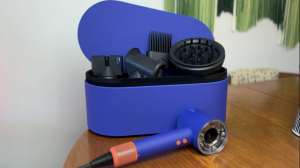 Dyson Supersonic Nural hair dryer laying on a table with the case of all attachments behind it.